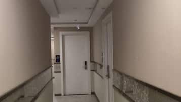 A corridor with a door at the end, a handrail on the left, and a wall-mounted light fixture.