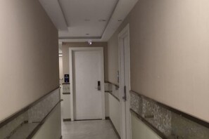 Un couloir avec une porte au fond, une main courante à gauche et un luminaire fixé au mur.