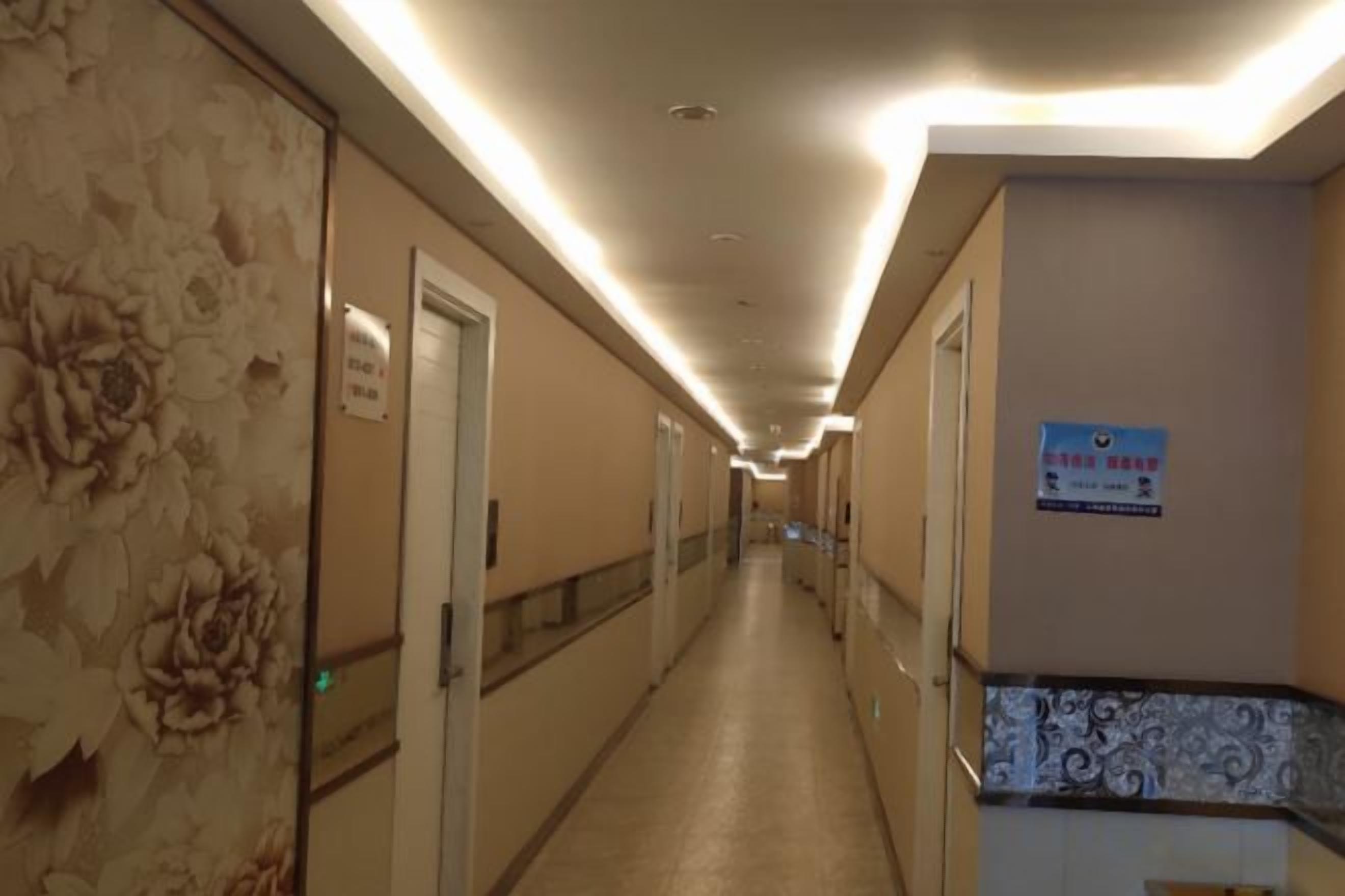 A hotel corridor with doors on both sides, a sign on the right wall, and a patterned wall on the left.