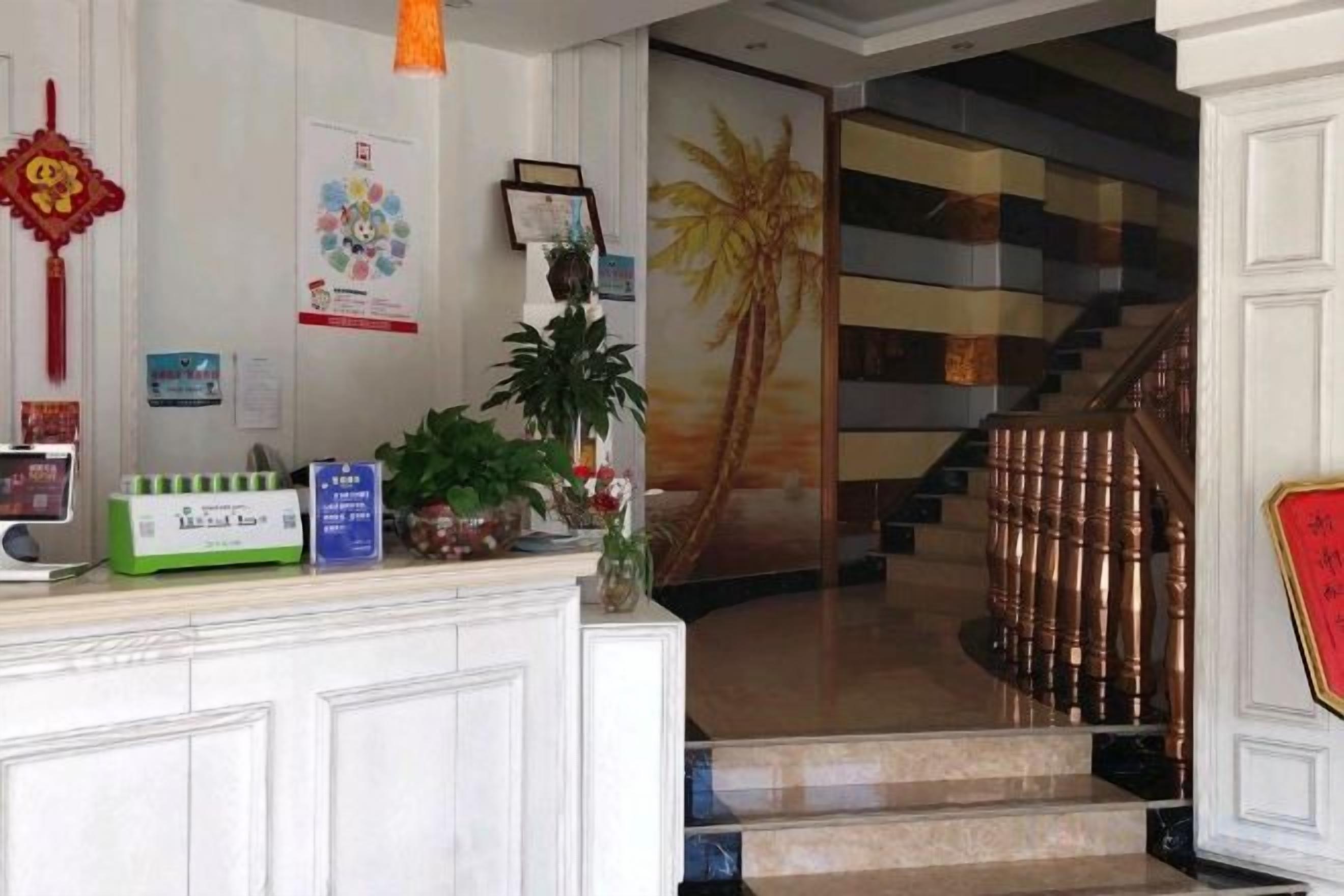 A hotel reception area with a reception desk, a staircase, and a palm tree mural.