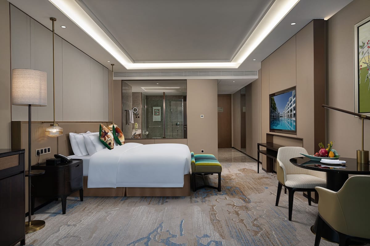 A hotel room with a large bed, bedside tables, a desk, a chair, a lamp, and a television.