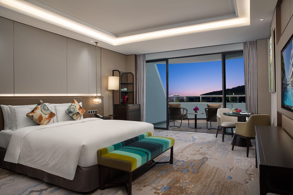 Habitación de hotel con una cama grande, un escritorio, una silla, una mesita y un balcón con vistas.