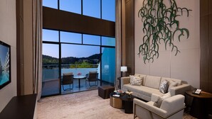 Ein modernes Hotelzimmer mit einer großen Glasschiebetür, die auf einen Balkon führt, einer Sofagarnitur, einem kleinen Tisch und einem dekorativen Wandbild.