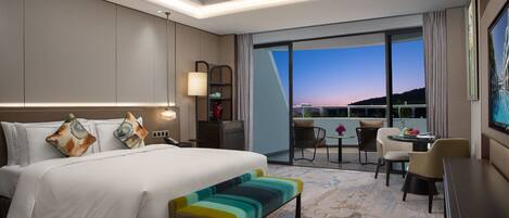 Una habitación de hotel moderna con una cama grande, un escritorio y un balcón con vistas al horizonte de la ciudad.