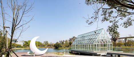 A park with a glass greenhouse structure, a crescent moon sculpture, and a lake.