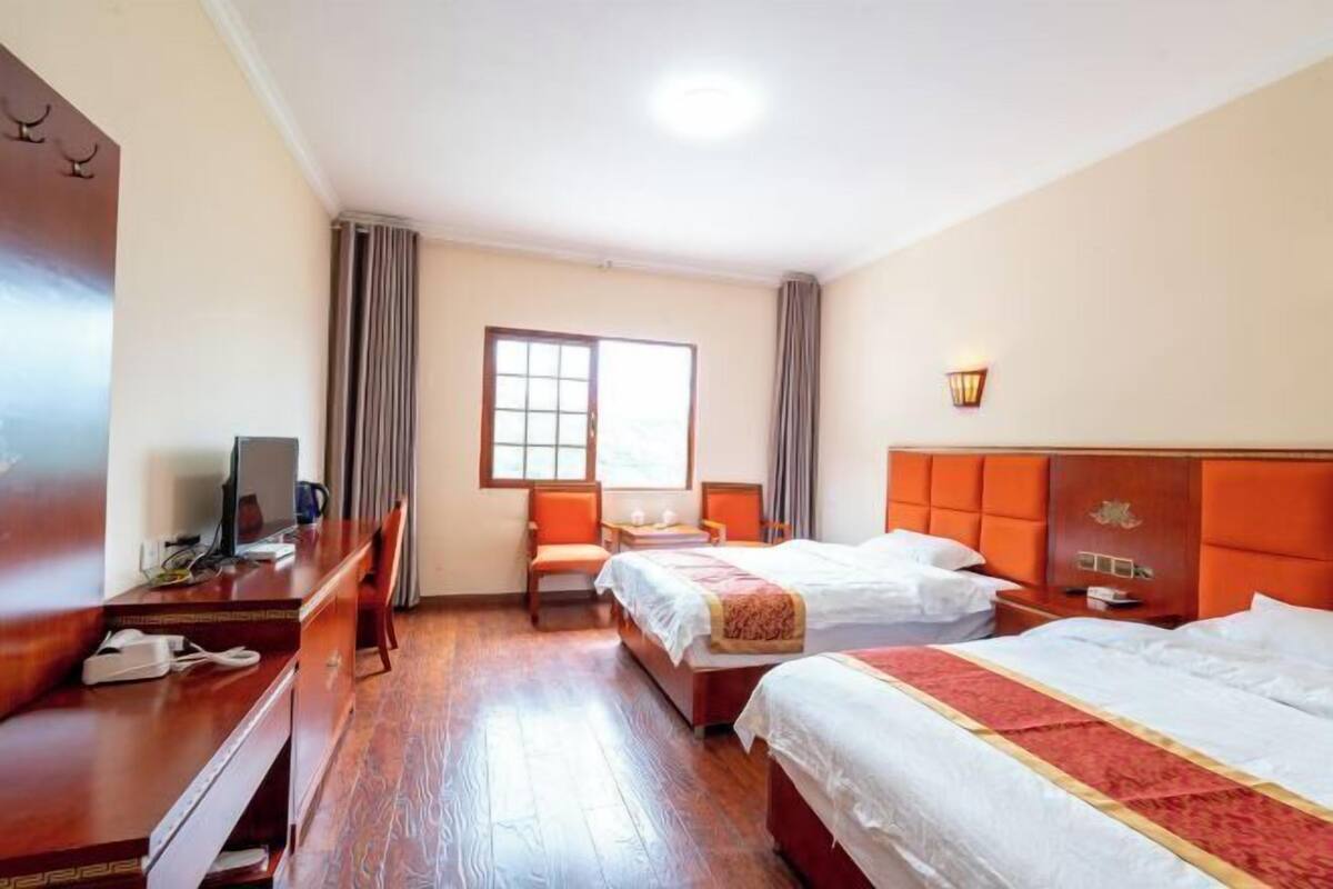 Une chambre d’hôtel avec deux lits, un bureau, une chaise, une télévision et une fenêtre avec des rideaux.