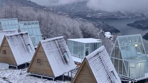 Une rangée de cabanes en bois dotées de toits en verre, se dressant sur un fond de montagnes et bordant un plan d’eau.