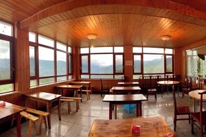 A wooden interior with tables and benches, large windows, and a view of mountains.