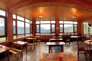 Un interior de madera con mesas y bancos, ventanas amplias y vistas a montañas.