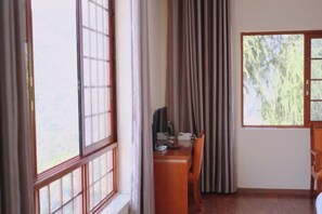 Ein Zimmer mit einem Holztisch, einem Stuhl, einem Vorhangfenster und Blick auf Grün.