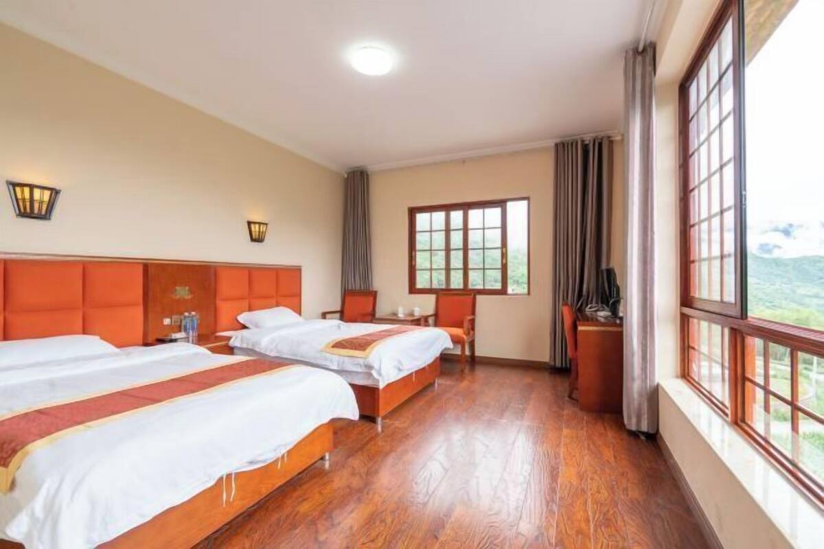 Une chambre d’hôtel avec deux lits, un bureau, une chaise, une télévision et de grandes fenêtres donnant sur un beau paysage.