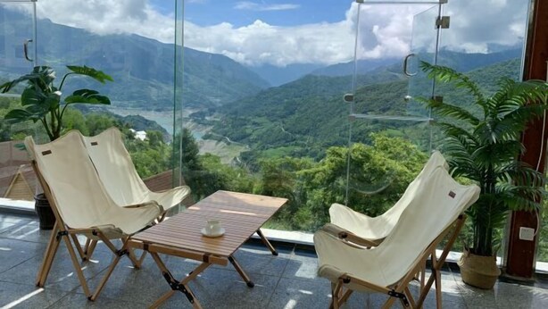 Une pièce dotée d’un mur en verre donnant sur les montagnes, de deux fauteuils confortables, d’une petite table en bois et d’une plante en pot.