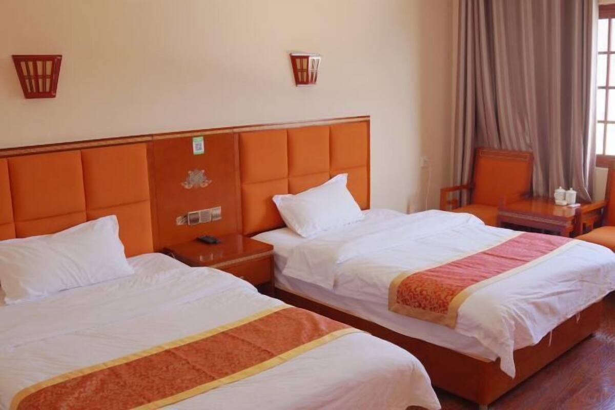 Une chambre d’hôtel avec deux lits, une tête de lit en bois, une table de chevet, une chaise et une fenêtre avec des rideaux.