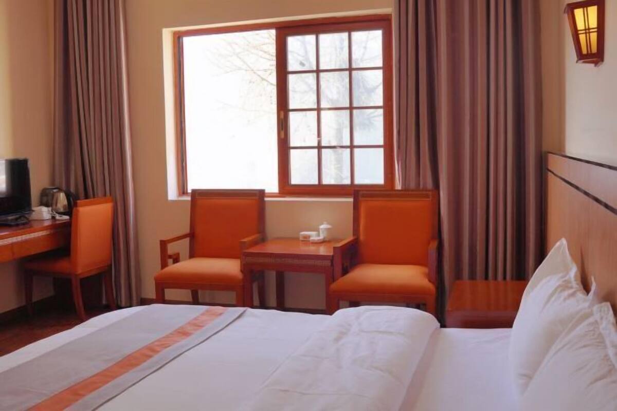 Une chambre d’hôtel avec un lit, deux chaises, une petite table, un téléviseur et une fenêtre avec des rideaux.