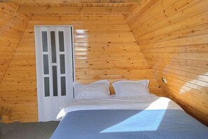 Ein kleiner Raum mit Holzwänden, einem Bett, einer Glastür und einer geneigten Decke.