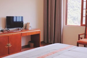 Ein Hotelzimmer mit Bett, Schreibtisch mit Fernseher, Stuhl und einem Fenster mit Vorhängen.