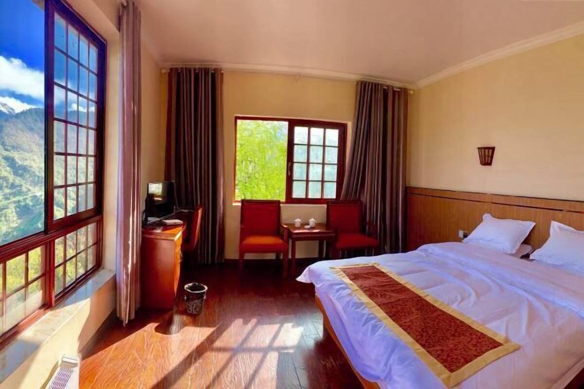 Une chambre d’hôtel avec un grand lit, un bureau, deux chaises et une vue sur les montagnes par la fenêtre.