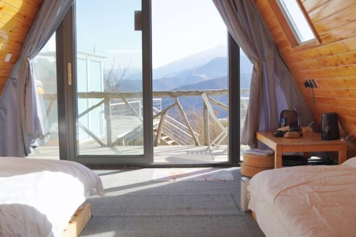 Une chambre avec deux lits, une table en bois et une grande porte-fenêtre coulissante donnant sur une terrasse extérieure.