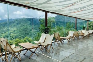 Una terraza con sillas y mesas, ventanas amplias y vistas a un paisaje verde.