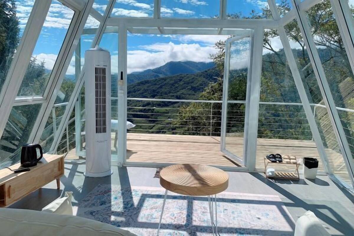 Une pièce dotée d’une grande fenêtre, d’un banc en bois, d’une petite table ronde et d’un appareil de climatisation blanc.