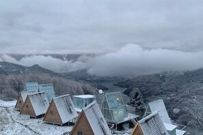 Eine Reihe von Holzhütten mit Glasdächern, vor einer Berglandschaft mit See und Wolken.