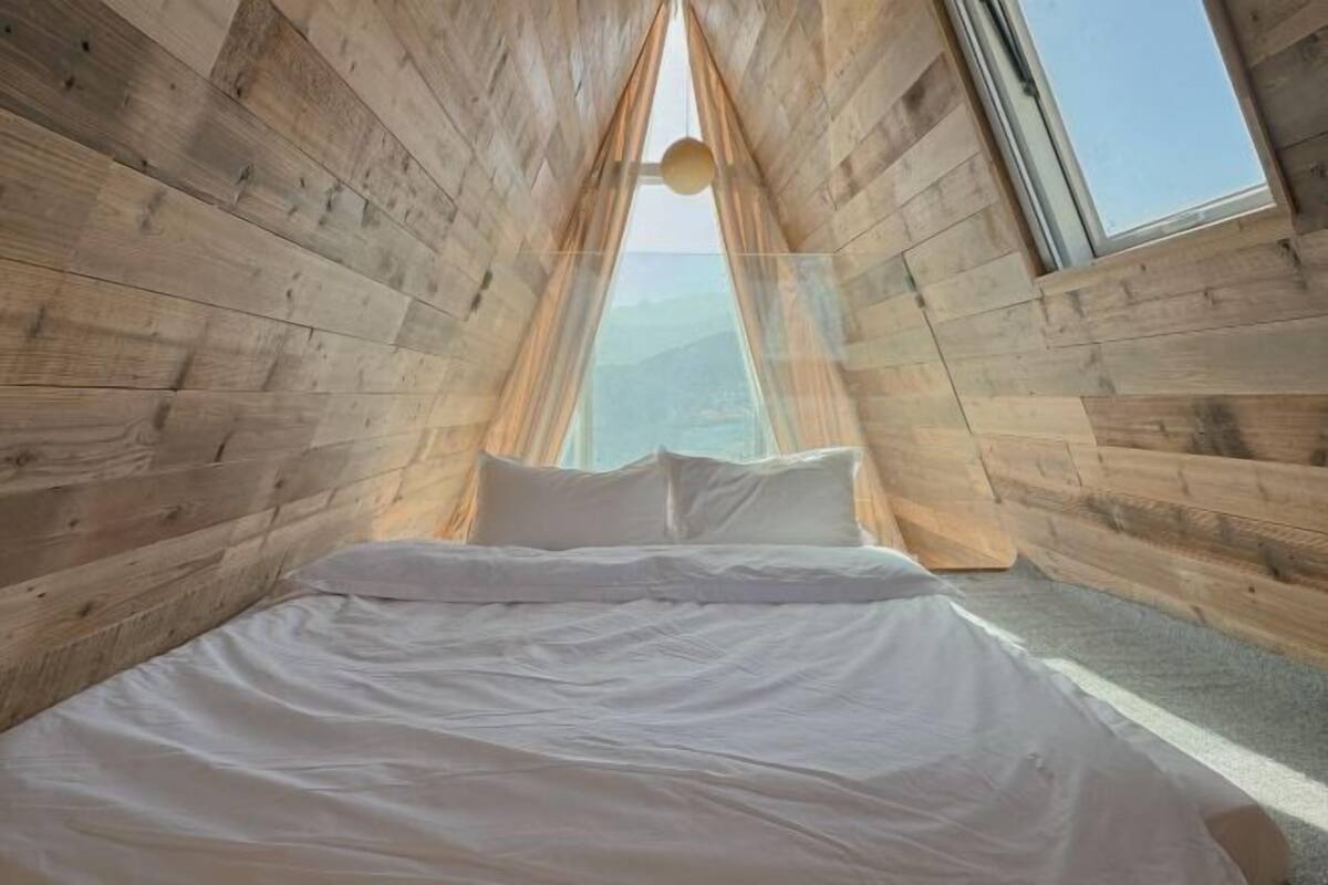 Une pièce avec un lit, des murs en bois et une fenêtre.