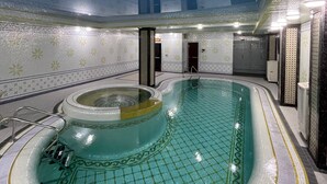 Una piscina interior con suelo de baldosas y una zona de hidromasaje central.
