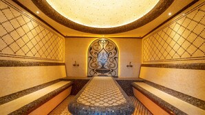 Un área de spa con un banco central, paredes de mosaico y una lámpara circular en el techo.