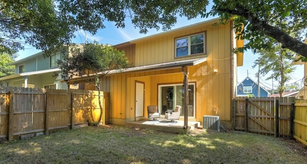 A two-story house with a covered patio, a fenced backyard, and a tree providing shade.