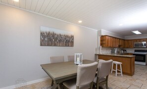 Un coin repas avec une table et des chaises en bois, un tableau accroché au mur, et une cuisine dotée de meubles et d’appareils électroménagers en bois.
