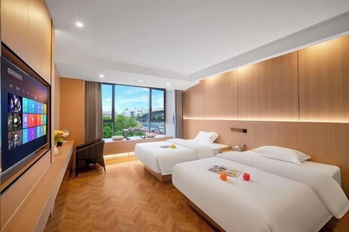 Een hotelkamer met twee bedden, een televisie aan de muur en een groot raam met uitzicht op de stad.