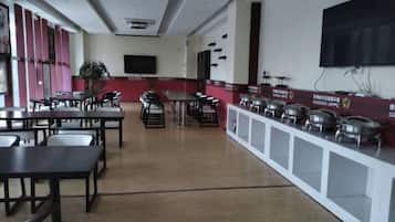 A cafeteria with tables and chairs, a television mounted on the wall, and a counter with food containers.