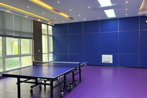 Une table de ping-pong dans une pièce dotée de grandes fenêtres et d’un mur bleu.