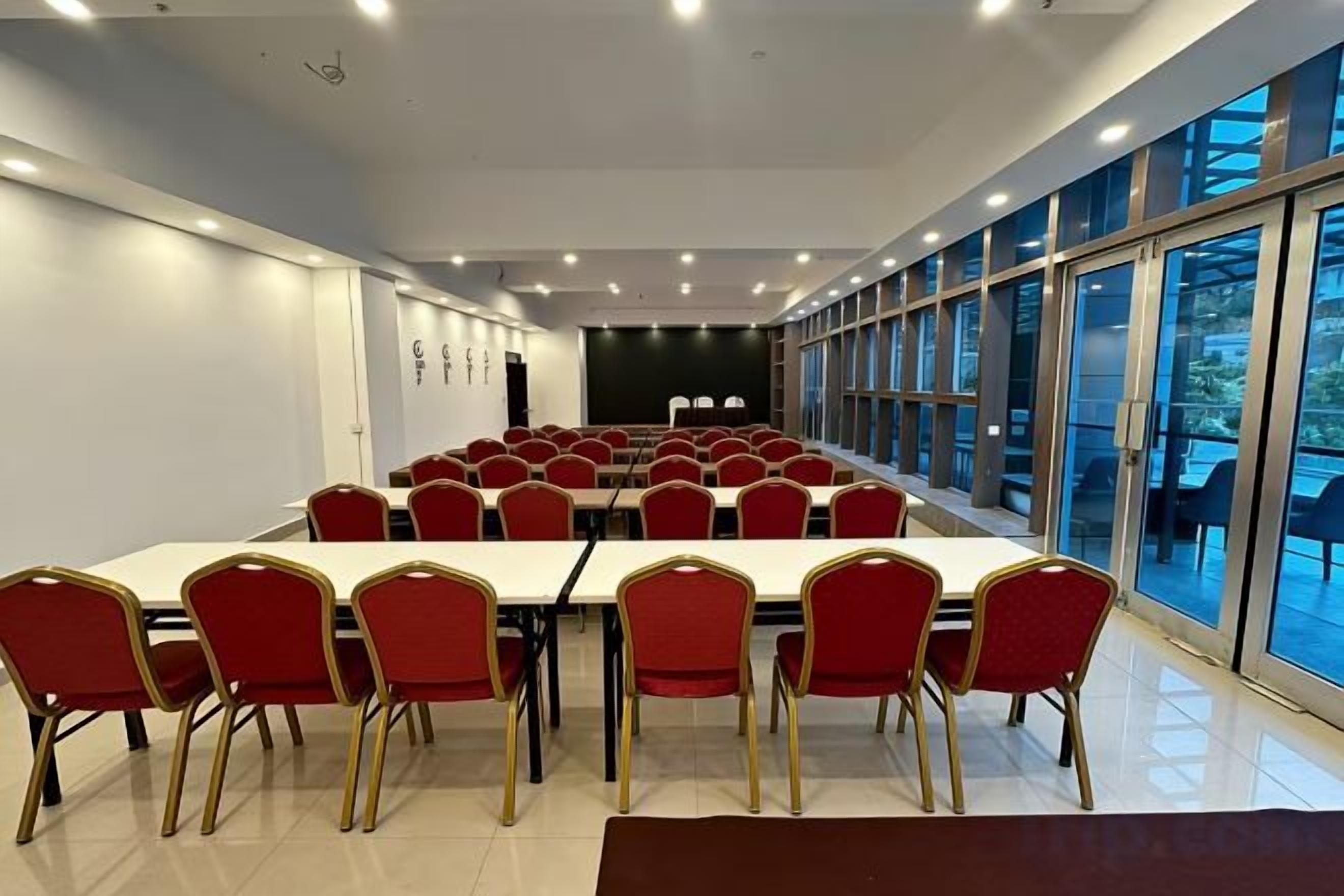 A conference room with a long table and red chairs, large windows, and a stage.