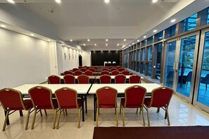 Une salle de conférence avec une longue table et des chaises rouges, de grandes fenêtres et une scène.