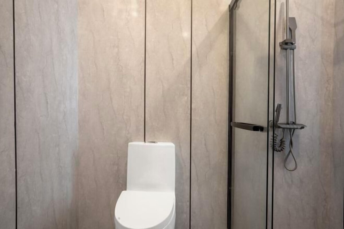 A modern bathroom with a white toilet, a glass-enclosed shower, and marble walls.