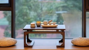 Uma pequena mesa de madeira com objetos de cerâmica e almofadas trançadas em frente a uma janela.