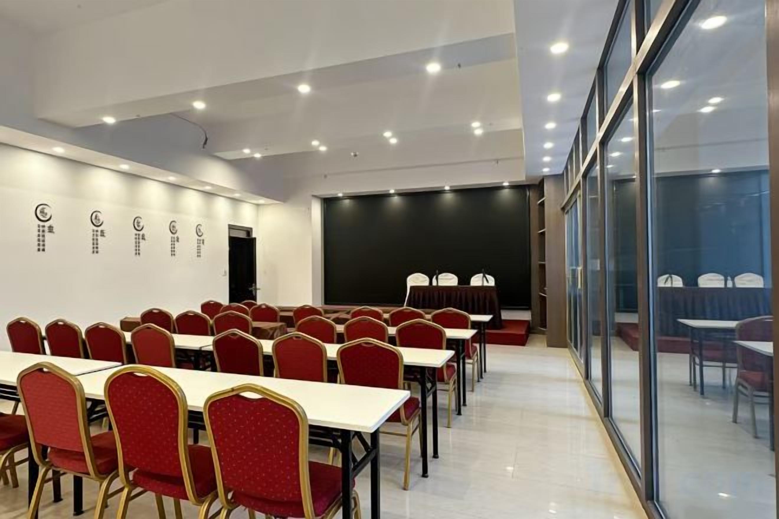 A conference room with rows of tables and chairs, a stage, and a large screen.