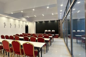 Une salle de conférence avec des rangées de tables et de chaises, une scène et un grand écran.
