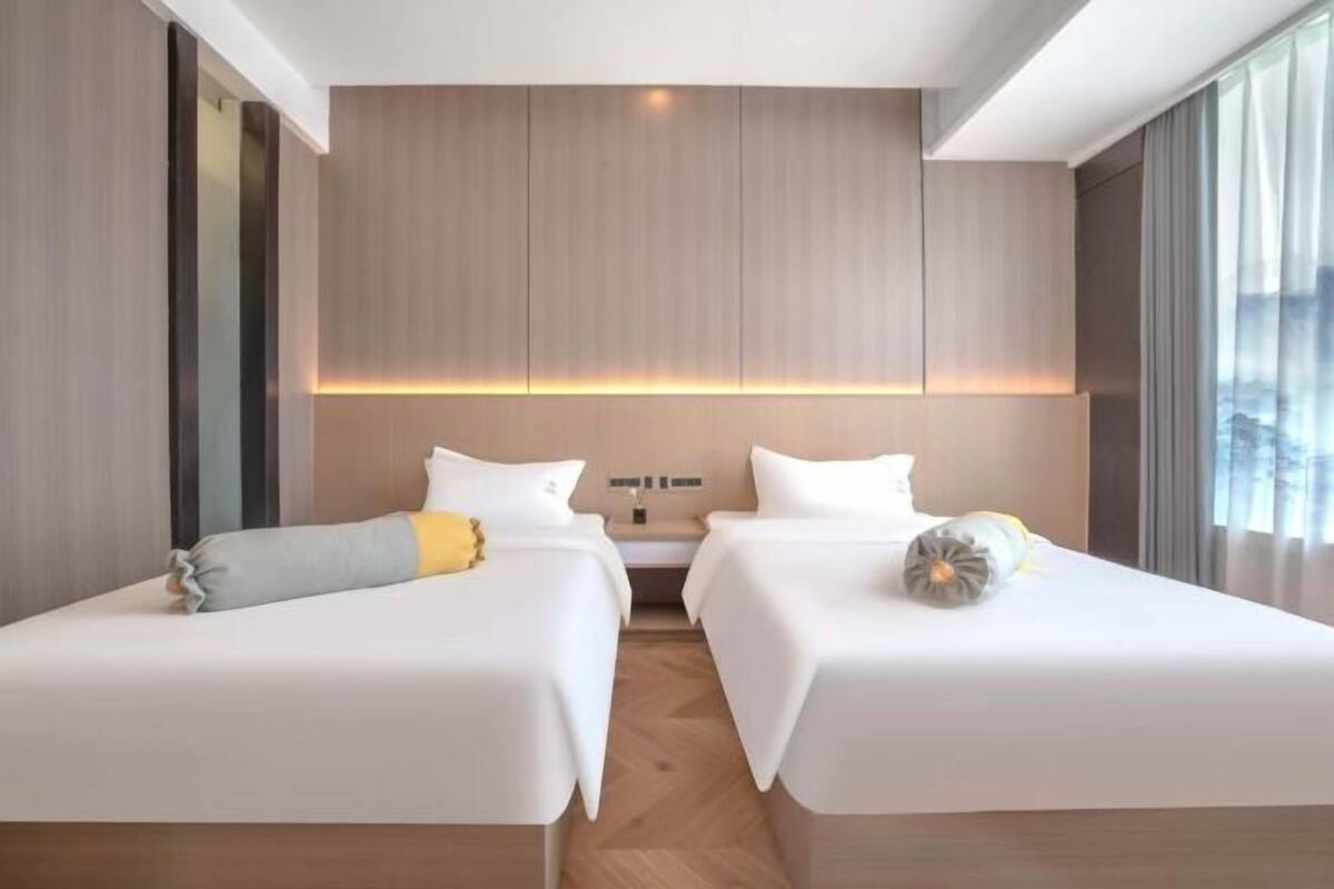 Een hotelkamer met twee bedden, een houten hoofdeinde en uitzicht door grote ramen.