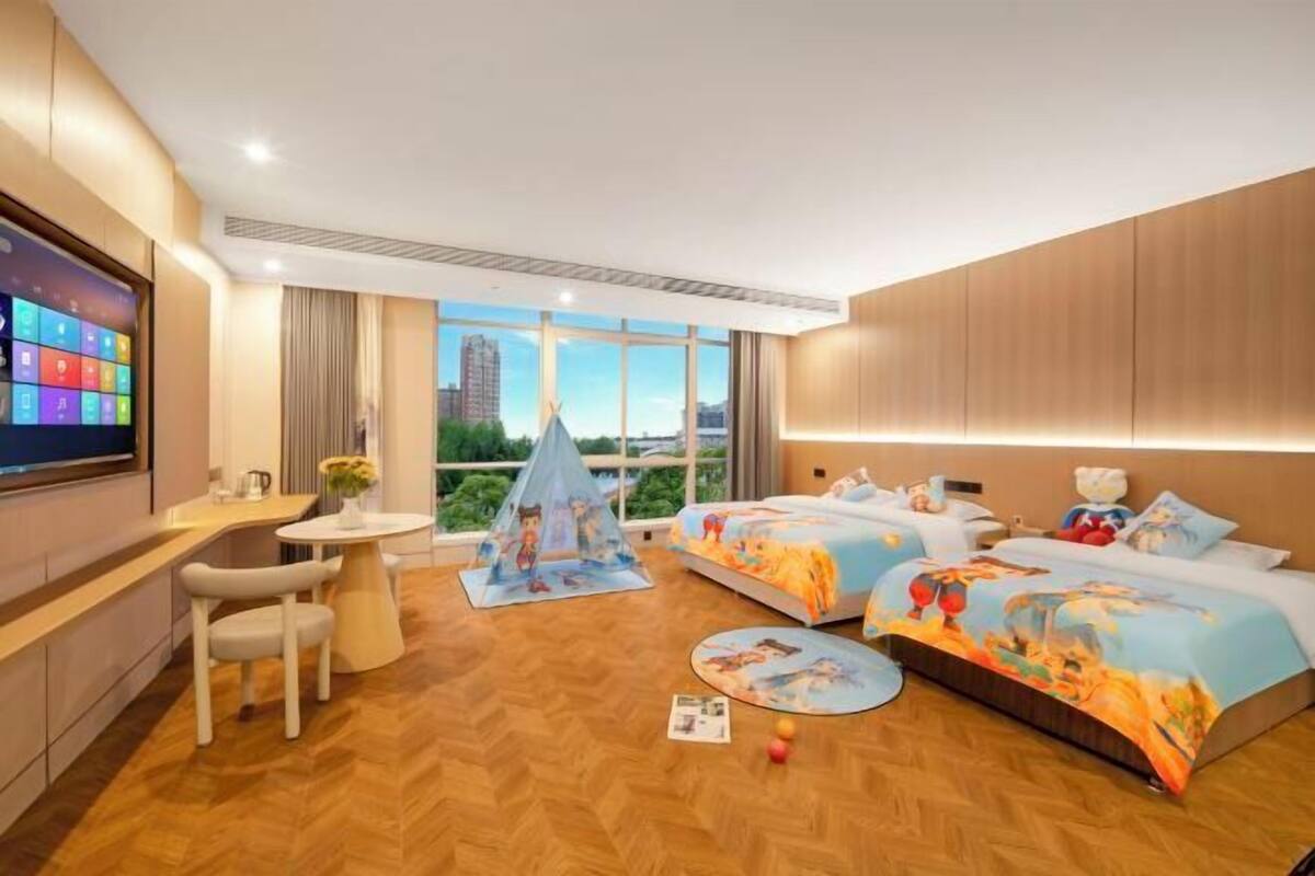Hotelkamer met twee bedden, een bureau, een stoel, een kleine tafel en een groot raam met uitzicht op de stad.