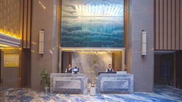 Ein Hotel-Empfangsbereich mit einer großen digitalen Kunstausstellung, Empfangstheken und einem Marmorboden.