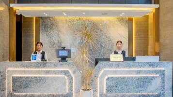 A reception desk with two receptionists, a digital screen, and a potted plant.