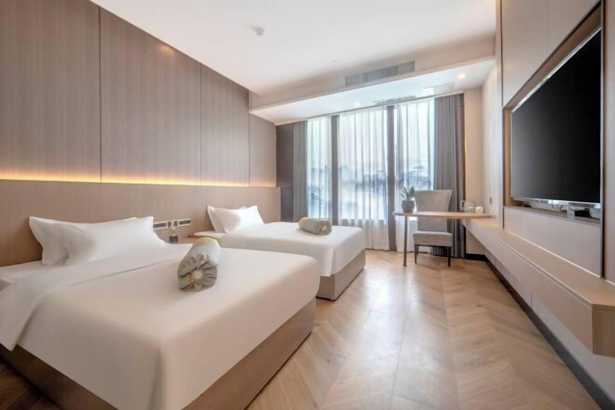 Een hotelkamer met twee bedden, een bureau, een stoel, een televisie en een groot raam met gordijnen.