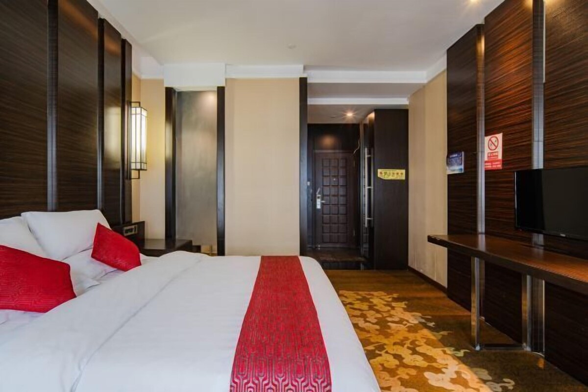 A hotel room with a bed, a TV, a desk, and a door leading to a hallway.