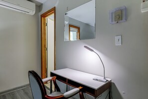 Ein Zimmer mit Schreibtisch, Stuhl, Spiegel und einer Wandleuchte.