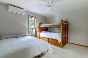 Un dormitorio con una litera, una cama individual, un ventilador de techo y una ventana con vistas a árboles.