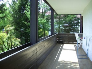 A balcony with a wooden floor, a metal clothes rack, and a view of trees and buildings.
