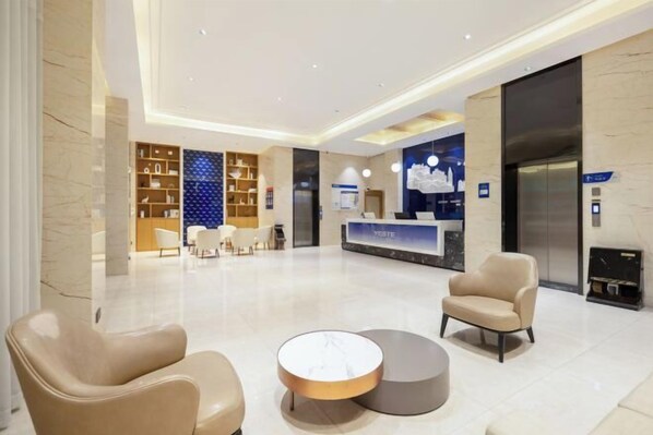 Un hall d’hôtel moderne comprenant un comptoir d’accueil, un espace salon et un ascenseur.