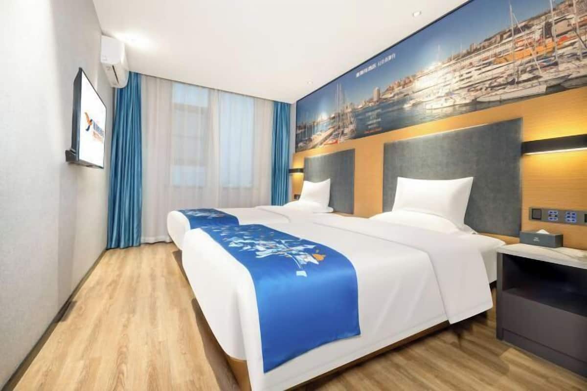 Ein Hotelzimmer mit einem großen Bett, einem Nachttisch, einer an der Wand befestigten Bedienkonsole und einem großen Fenster mit Vorhängen.